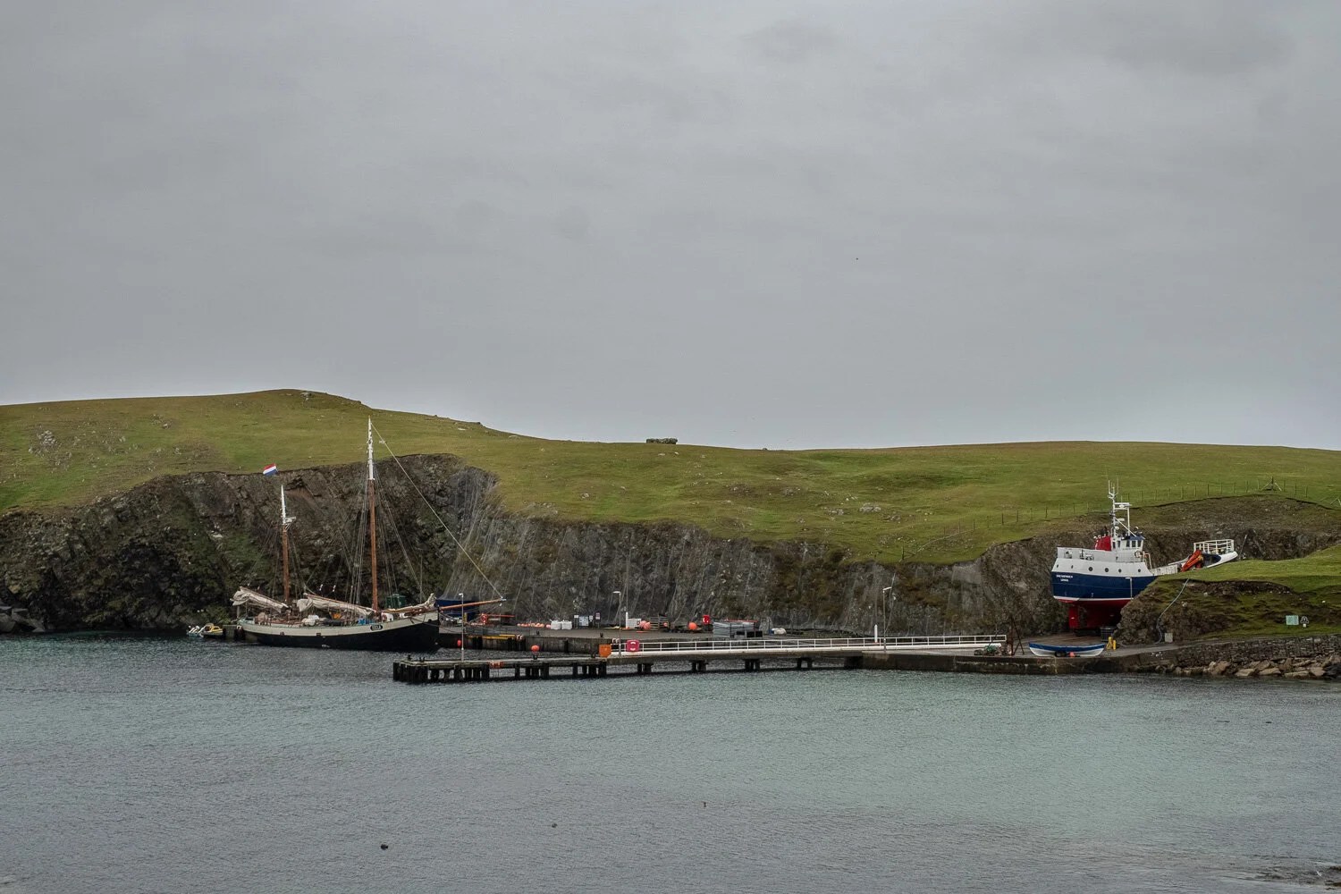  Tecla moored at the only dock on Fair Isle. Ferry in dry dock waiting to get to its mooring. Tiny black dots to the bottom left are seal heads watching our activity. 